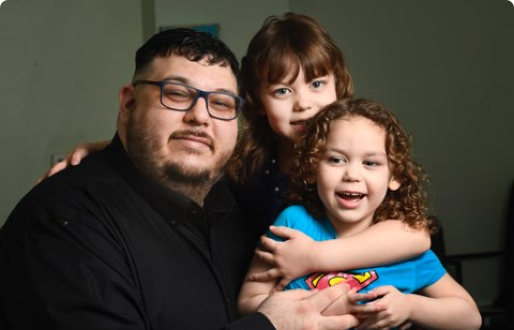 Photograph of Adam Longboat and his two daughters smiling at the camera